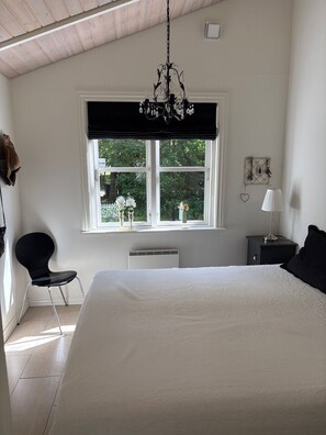 Ein Schlafzimmer mit einem großen Bett, einem Fenster mit Blick auf Grünflächen, einem Sessel, einem Nachttisch und einer Lampe.
