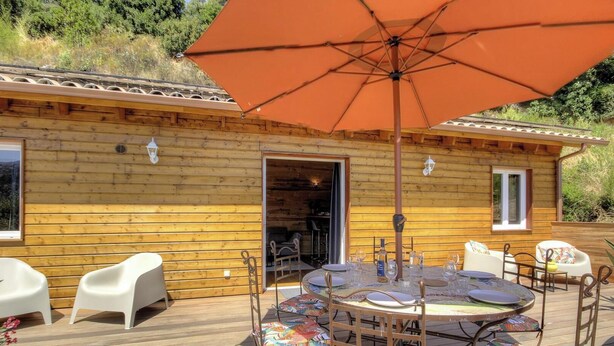 Una cabaña de madera con comedor, zona de estar exterior y una sombrilla grande.