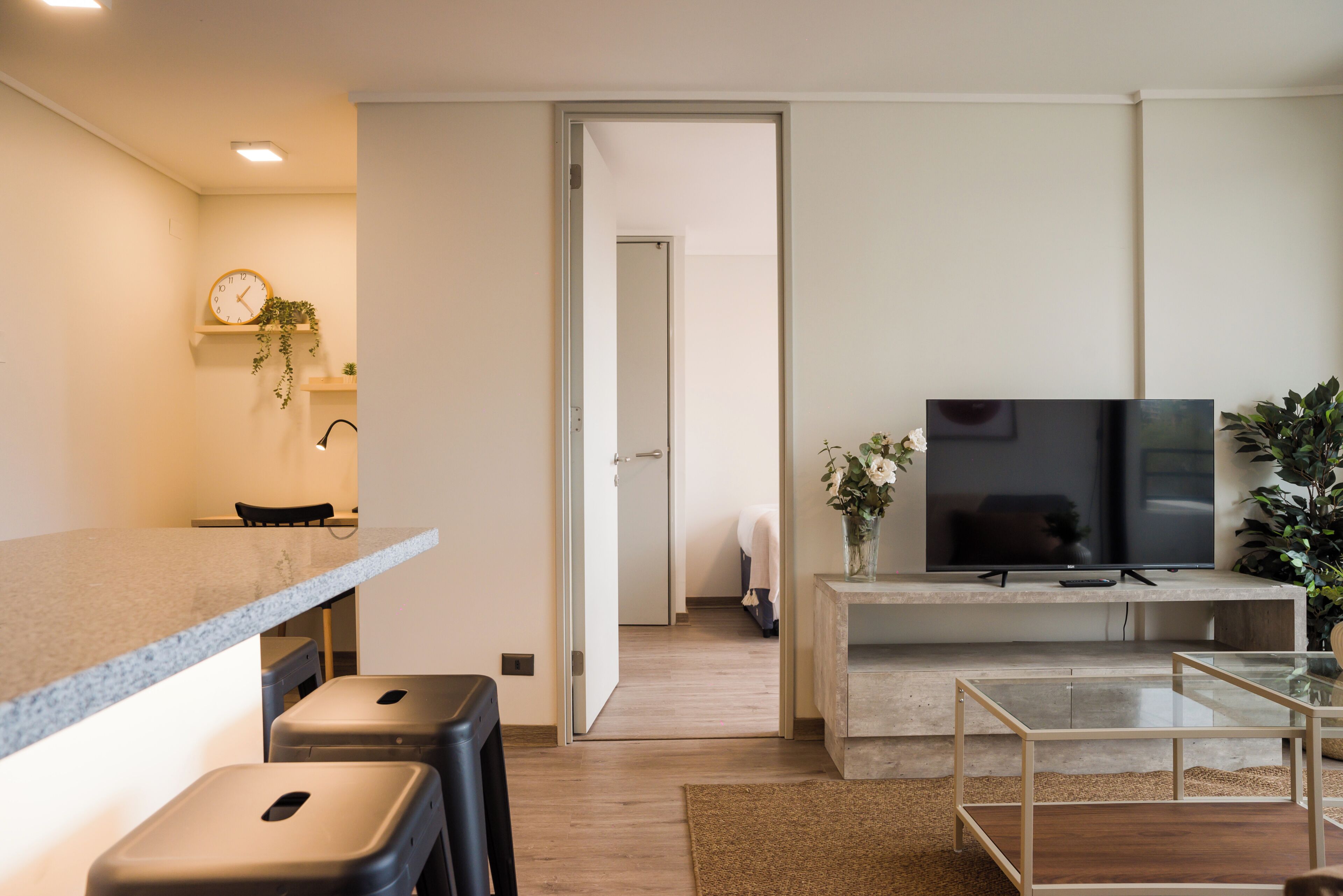 Una sala moderna con un televisor de pantalla plana, una mesa de centro y una zona de estar con taburetes.