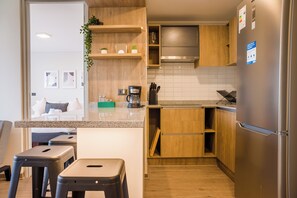 A modern kitchen with wooden cabinets, a stainless steel refrigerator, and a coffee maker. - Beautiful Apt in Las Condes with Pool (Las Condes)