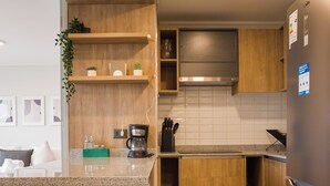A modern kitchen with wooden cabinets, a stainless steel refrigerator, and a countertop with a coffee maker and a plant. - Beautiful Apt in Las Condes with Pool (Las Condes)