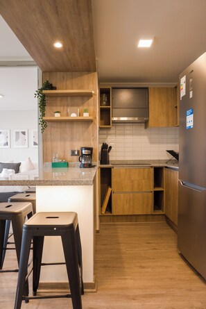 Eine moderne Küche mit Holzschränken, einem Edelstahlkühlschrank und einer Arbeitsplatte mit Kaffeemaschine und einer Pflanze.