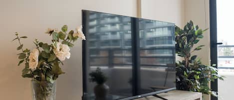 A flat-screen TV on a wooden console table with two vases of flowers.