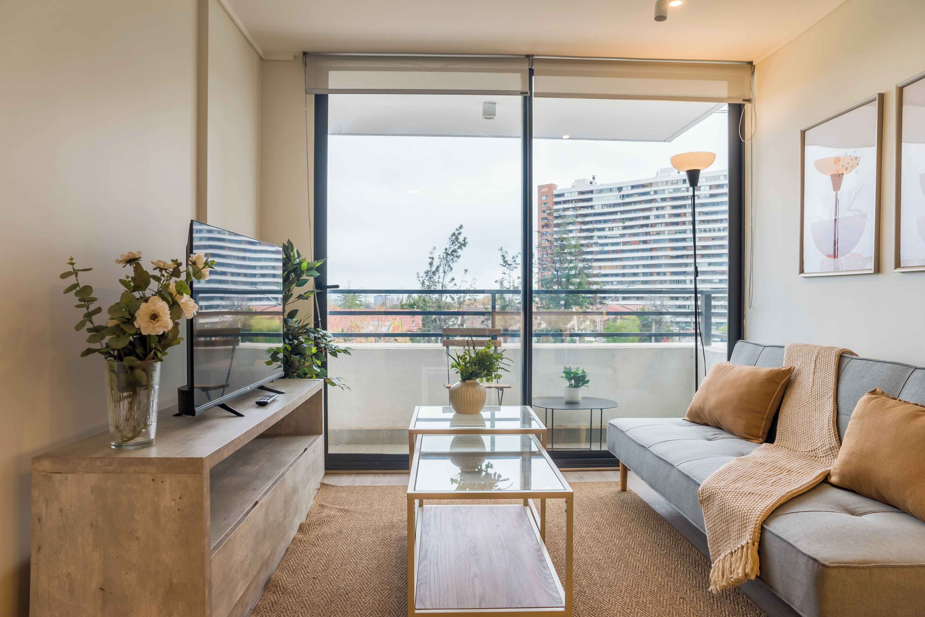 A modern living room with a sofa, coffee table, TV, and a balcony with a city view.
