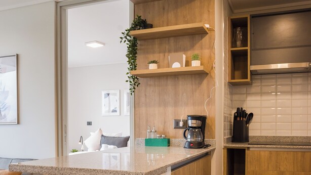 A modern kitchen with a wooden countertop, a coffee maker, and a plant on the shelf. - Beautiful Apt in Las Condes with Pool (Las Condes)