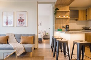 A modern apartment with a grey sofa, a coffee machine, and a kitchen with wooden cabinets. - Beautiful Apt in Las Condes with Pool (Las Condes)