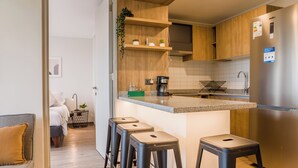 A modern kitchen with a central island, bar stools, a coffee maker, and a stainless steel refrigerator. - Beautiful Apt in Las Condes with Pool (Las Condes)