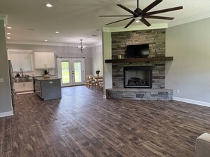 A spacious living area with a stone fireplace, a ceiling fan, and a dining area with a view to the outdoors.