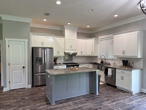 A modern kitchen with white cabinetry, a stainless steel refrigerator, and a granite countertop island.