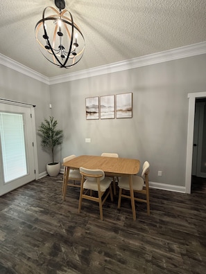 A dining room with a wooden table and chairs, a chandelier, and three framed pictures on the wall.