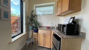 A compact kitchen with wooden cabinets, a granite countertop, a built-in microwave, a sink, and a potted plant.