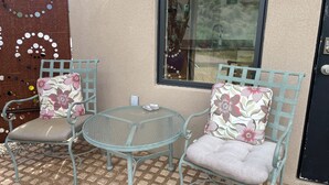 A small outdoor seating area with two chairs and a table, a window with a view, and a door with a keypad lock.