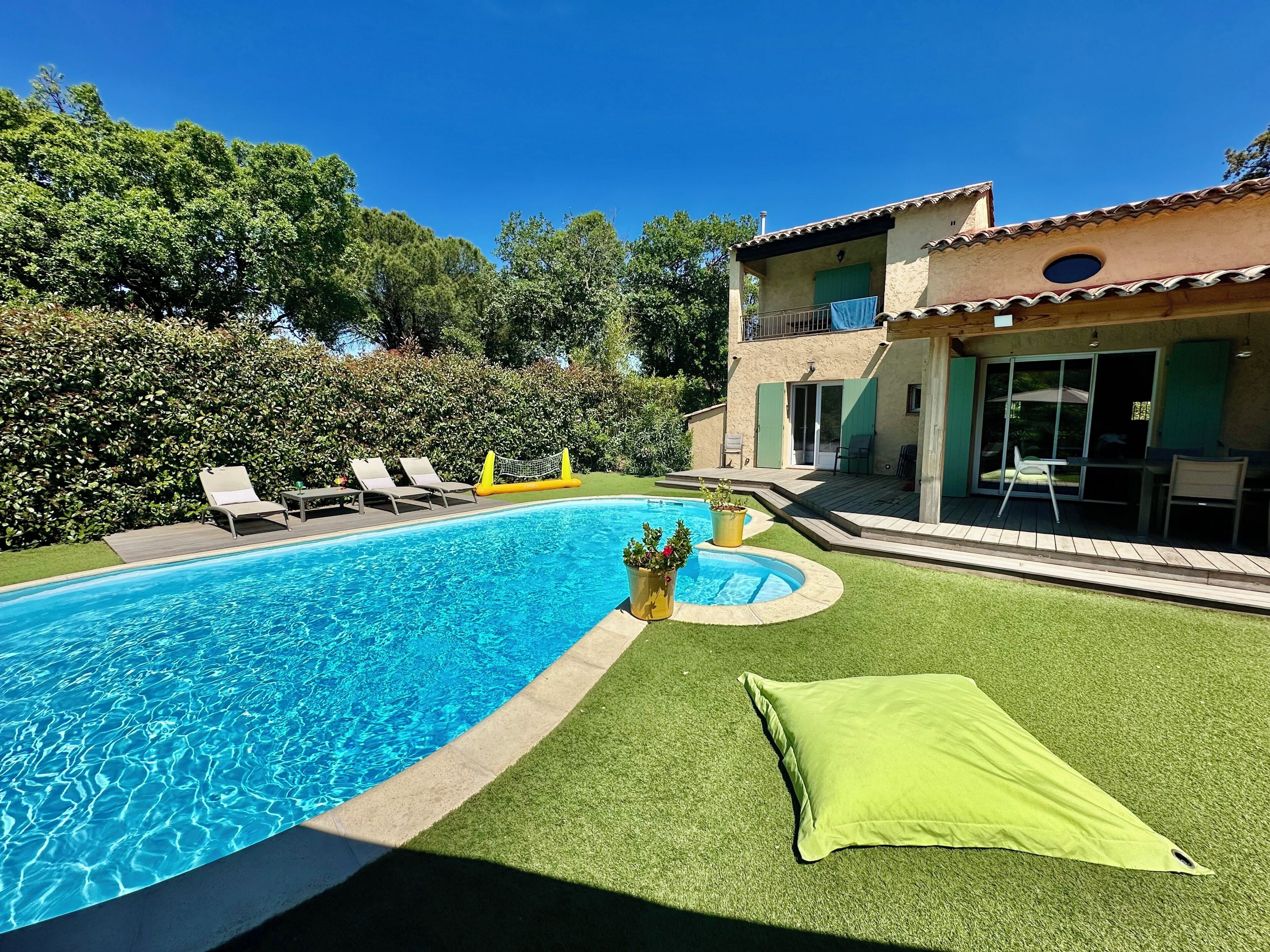 A swimming pool with a deck, lounge chairs, and a small garden area with a green lawn and potted plants.