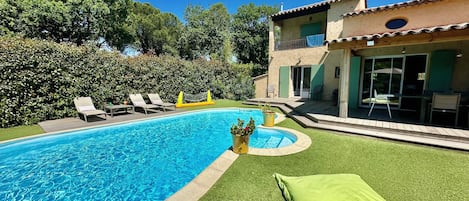 Una piscina con terraza, sillas de descanso y un pequeño jardín con césped verde y plantas en macetas.