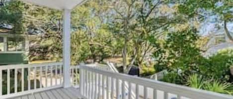 A wooden deck with a white railing overlooking a swimming pool and lush greenery.
