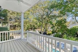 Eine Holzterrasse mit weißer Reling, die auf einen Swimmingpool und üppiges Grün blickt.