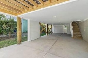 Ein großzügiger überdachter Außenbereich mit Betonboden, Holzträgern und einer Treppe, die zu einer Garage führt.