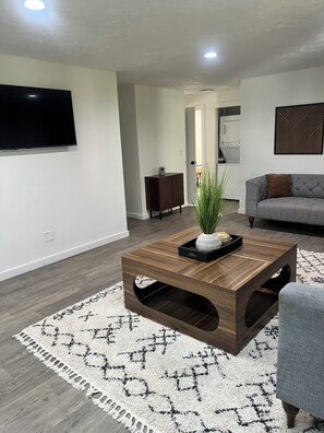 A modern living room with a flat-screen TV, a wooden coffee table, a grey sofa, and a patterned rug. - Charming 3 Bedroom Escape (Benton Harbor)