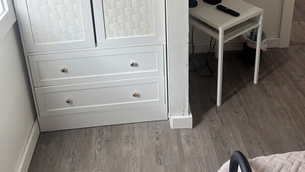 Ein Zimmer mit einem weißen Kleiderschrank, einem an der Wand befestigten Fernseher und einem kleinen Tisch mit einer Fernbedienung.
