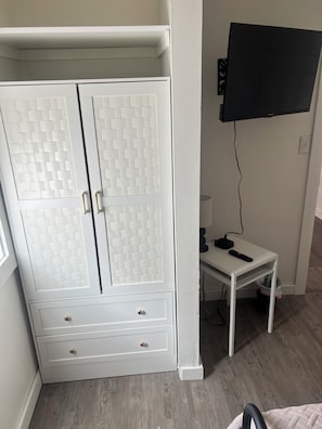 A room with a white wardrobe, a television mounted on the wall, and a small table with a remote control. - Charming 3 Bedroom Escape (Benton Harbor)
