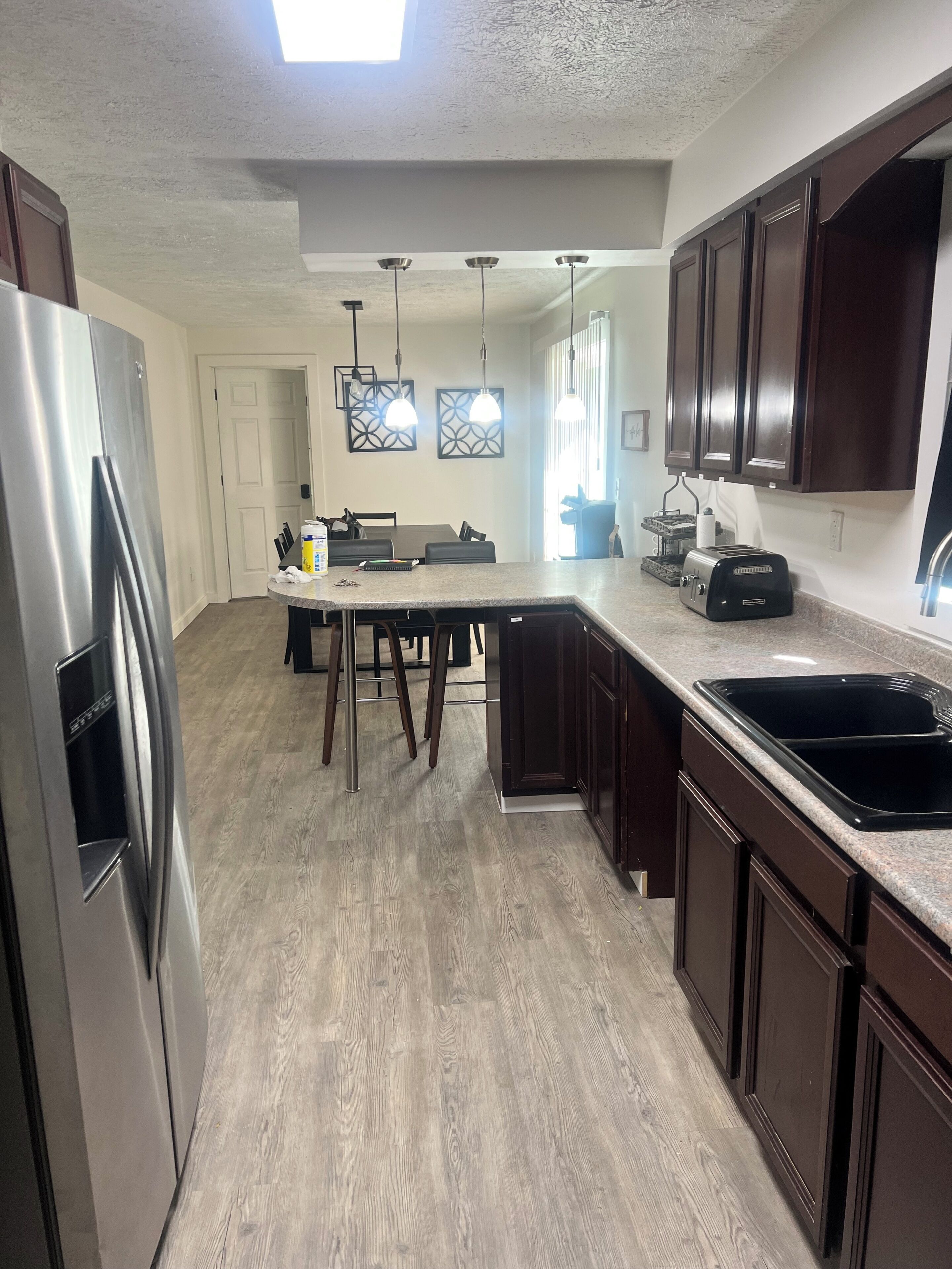 A kitchen with a stainless steel refrigerator, wooden cabinets, a granite countertop, and a dining area with a table and chairs.