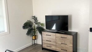 Ein Schlafzimmer mit einem Bett, einem Fernseher auf einer Holzkommode, einer Topfpflanze und einem Fenster.