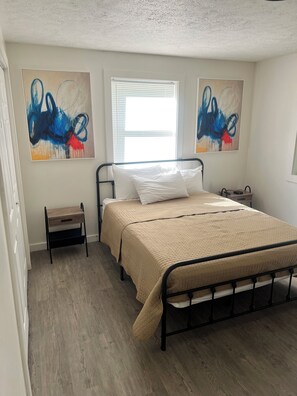 A bedroom with a bed, bedside tables, a window with blinds, and abstract wall art. - Charming 3 Bedroom Escape (Benton Harbor)