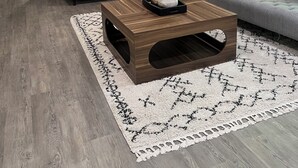Ein modernes Wohnzimmer mit einem Holztisch, grauen Sofas und einem großen Fenster mit Vorhängen.
