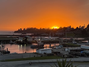 A marina with boats docked, a building with a red roof, and a sunset in the background.