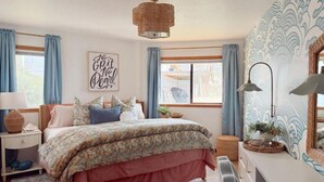 A bedroom with a bed, a nightstand, a lamp, a mirror, and a window with curtains. - The White Haus (Brookings)