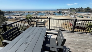 A wooden deck with a table and chairs, overlooking a marina with boats and a distant shoreline. - The White Haus (Brookings)