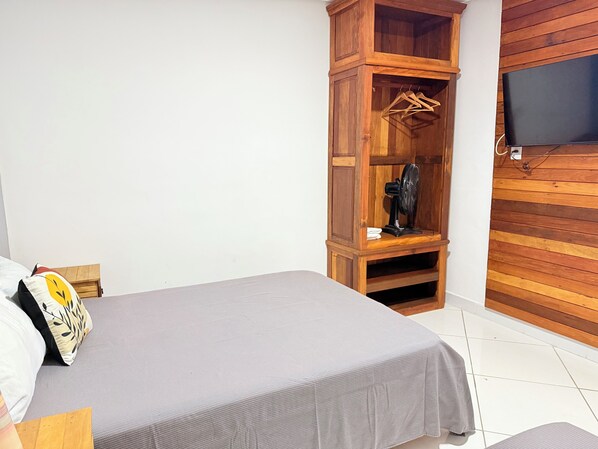 A bedroom with a bed, a wooden wardrobe, a television, and a fan.