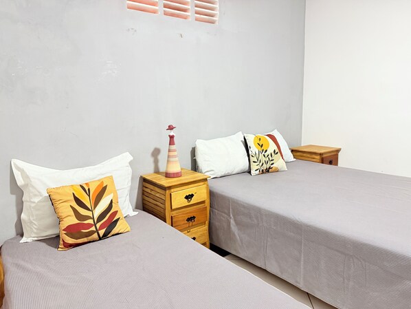 A room with two beds, each with a pillow and a bedside table.