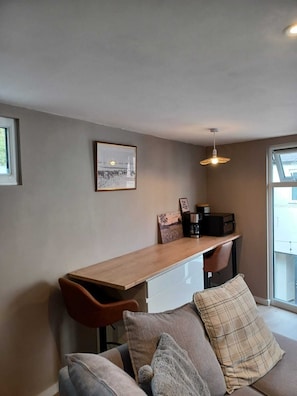 A modern living space with a long wooden table, a sofa with multiple cushions, and a framed picture on the wall.