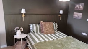 Un dormitorio con cama, lámparas de noche, una mesita con un jarrón y decoración en la pared.