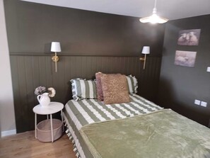 A bedroom with a bed, bedside lamps, a small table with a vase, and wall art.