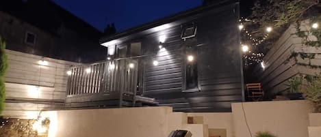 A modern two-story building with a balcony, outdoor seating, and string lights.