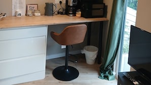 Una kitchenette funcional con cafetera, hervidor y microondas. Se observa una silla y un mueble bajo para televisión con control remoto.