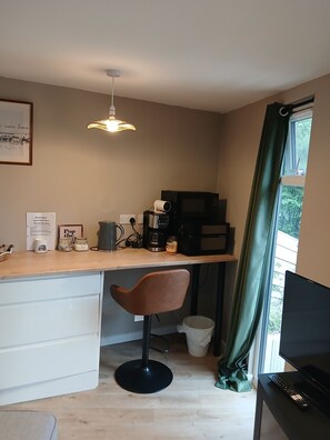 A compact kitchenette with a coffee maker, kettle, and microwave. There is a chair and a TV stand with a remote control.