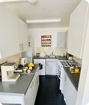 A compact kitchen with a gas stove, a coffee machine, a sink, and a small washing machine. - Stylish & Spacious 1BR flat- Central-Free Parking (London)