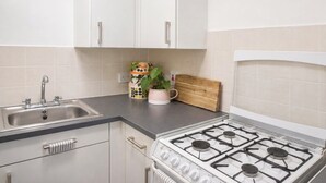 A kitchen with white cabinets, a stainless steel sink, a gas stove, and a wooden cutting board. - Stylish & Spacious 1BR flat- Central-Free Parking (London)