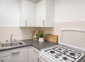 A kitchen with white cabinets, a stainless steel sink, a gas stove, and a wooden cutting board. - Stylish & Spacious 1BR flat- Central-Free Parking (London)