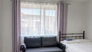 A bedroom with a bed, a sofa, and a window with curtains. - Stylish & Spacious 1BR flat- Central-Free Parking (London)