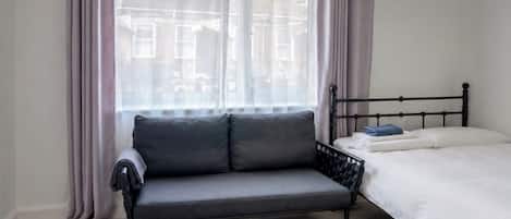 A bedroom with a bed, a sofa, and a window with curtains.