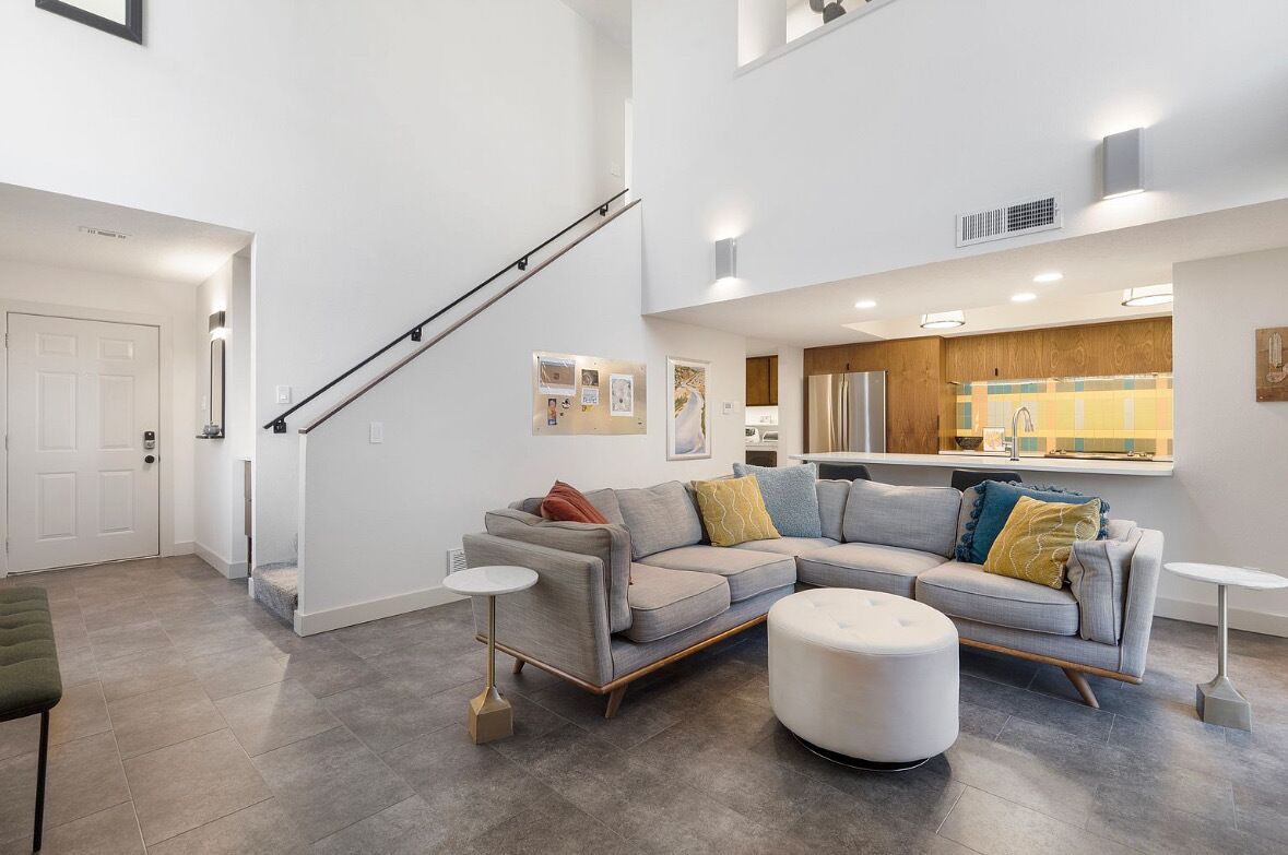 A modern living room with a sectional sofa, ottoman, and a staircase.