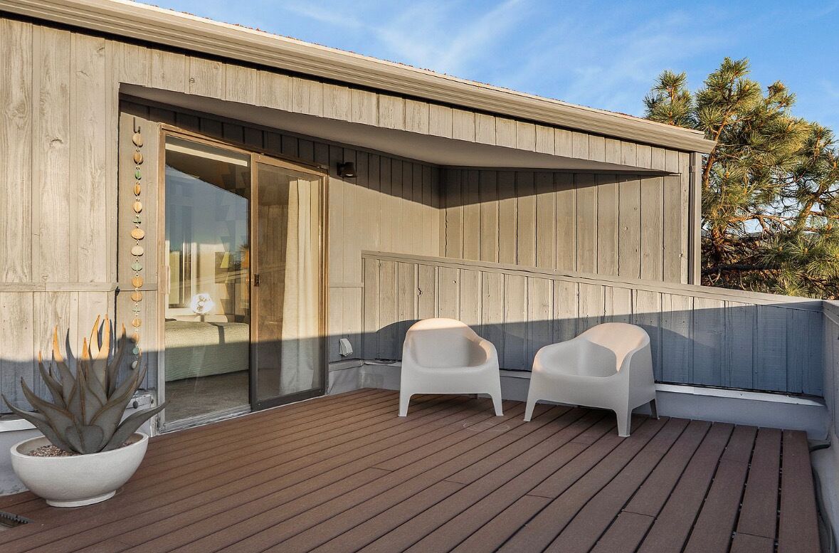 Una terraza de madera con dos sillas blancas y una planta en maceta.