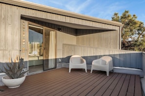 A wooden deck with two white chairs and a potted plant.