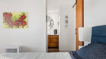 Une chambre à coucher avec un lit, une table de chevet, une lampe, un tableau et une vue sur la cuisine.
