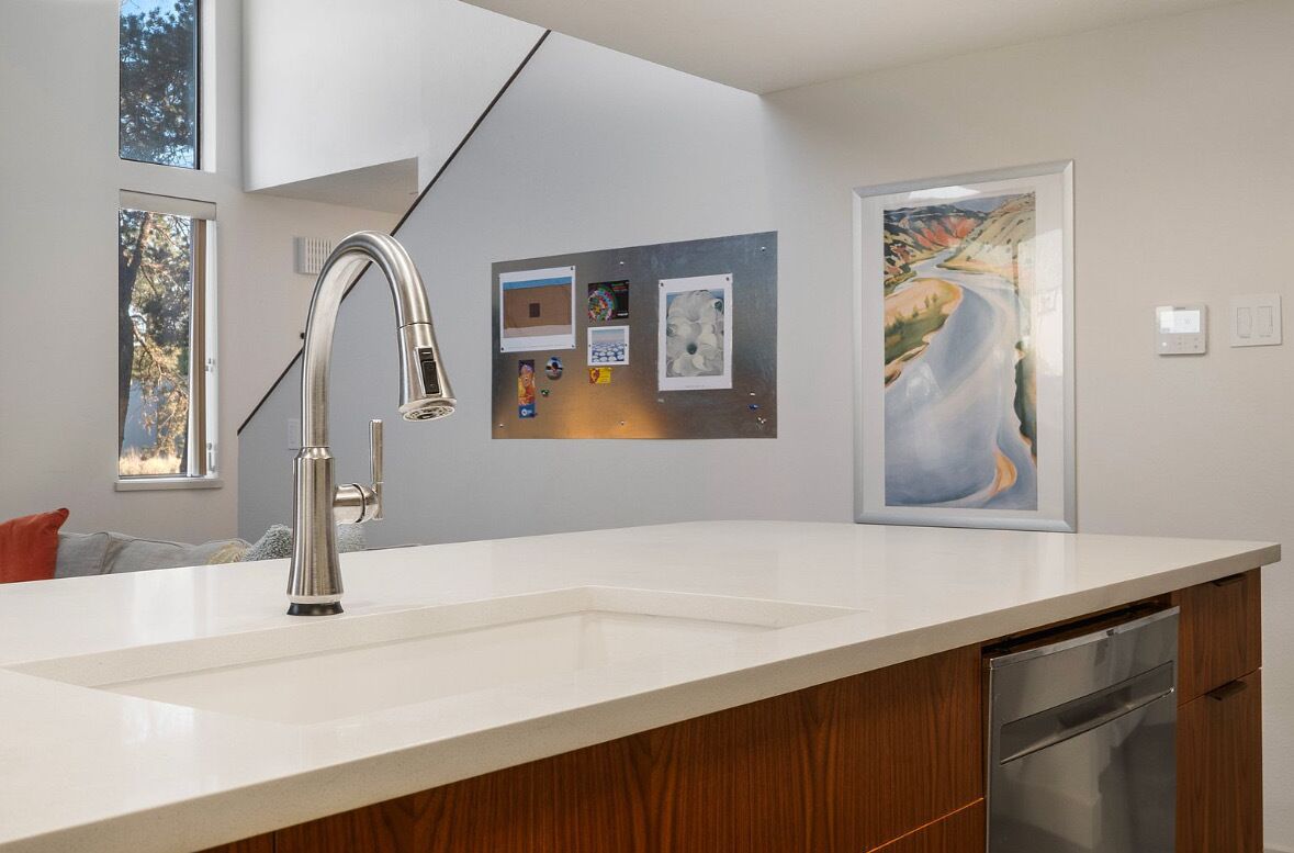 A modern kitchen with a stainless steel faucet, a white countertop, and a dishwasher. There are framed pictures on the wall.