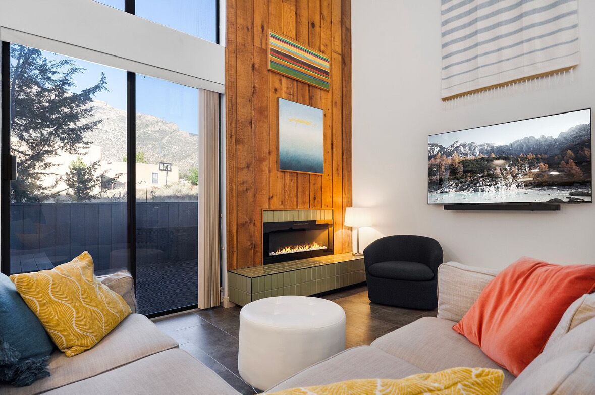 A modern living room with a fireplace, a large window, and a mounted TV.